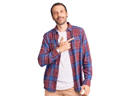 Genç, yakışıklı, günlük kıyafetler giyen, neşeli, yüzünde bir gülümseme olan, mutlu ve doğal bir ifadeyle elini ve parmağını kaldıran bir adam. 