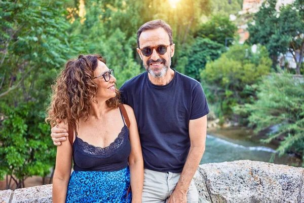 Pareja Mediana Edad Sonriendo Feliz Sentado Pared Piedra Mirando Cámara —  Fotos de Stock