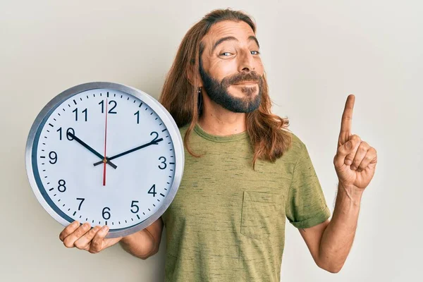 Привабливий Чоловік Довгим Волоссям Бородою Тримає Великий Годинник Посміхаючись Ідеєю — стокове фото