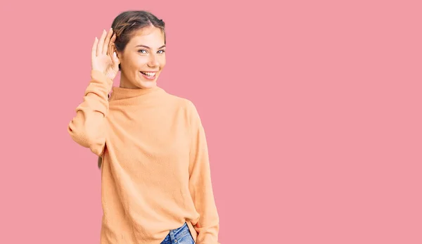 噂やゴシップに耳を傾ける耳の上に手で笑みを浮かべてカジュアルな冬のセーターを着てブロンドの髪を持つ美しい白人女性 聴覚障害の概念 — ストック写真