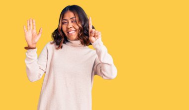 Genç ve güzel melez balıkçı yaka kazak giyen kadın altı numaralı parmaklarıyla gülümseyerek mutlu ve kendinden emin görünüyor.. 