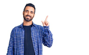 Yüzünde kocaman bir gülümseme olan, gündelik kıyafetler giyen genç İspanyol adam, kameraya el ile işaret ediyor.. 