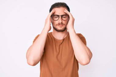 Genç yakışıklı adam günlük kıyafetler ve gözlük takıyor. Baş ağrısı, çaresiz ve stresli. Çünkü acı ve migren ağrısı var. Eller başının üstünde.. 