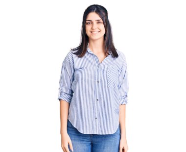 Çizgili gömlek giyen genç ve güzel bir kız. Pozitif ve mutlu görünüyor. Ayakta duruyor ve gülümsüyor. 