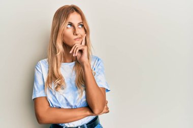 Tye die tişörtü giyen güzel sarışın kadın şüpheye odaklanmış, çenesinde parmak olan ve kafasını kaldırıp merakla bekleyen. 