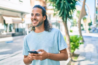 Genç İspanyol adam şehirde akıllı telefon kullanarak mutlu gülümsüyor..