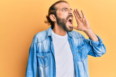 Uzun saçlı, sakallı, sıradan bir kot ceket giyen, el ve ağızla bağırıp çağıran çekici bir adam. iletişim konsepti. 