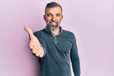 Orta yaşlı, sıradan kıyafetler giyen yakışıklı bir adam dostça bir selamlama ve hoş geldin hediyesi olarak el sıkışmayı sunuyor. başarılı iş. 
