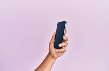 Soyutlanmış pembe arka planda akıllı telefon gösteren İspanyol bir adamın eli..