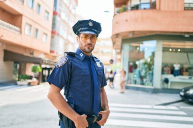 Polis üniforması giyen genç, yakışıklı İspanyol polis. Kasaba caddesinde ciddi bir ifadeyle dikiliyorsun..