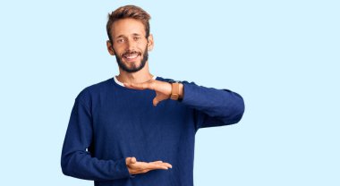 Sarışın, sakallı, sıradan kazak giyen, elleri büyük ve büyük boy işareti gösteren yakışıklı bir adam. Kameraya bakıp gülümsüyor. ölçüm kavramı. 