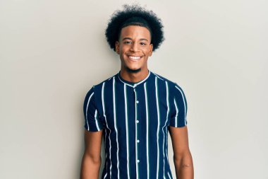 Afro saçlı, mutlu ve havalı bir gülümsemesi olan sıradan kıyafetler giyen Afro-Amerikan bir adam. şanslı kişi. 