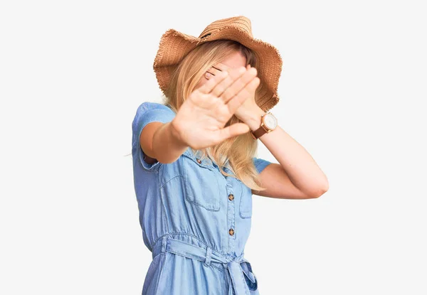 若い美しいブロンドの女性は夏の帽子をかぶって手で目を覆い 悲しいと恐怖の表情でジェスチャーを止めます 恥をかかせ否定的な概念 — ストック写真