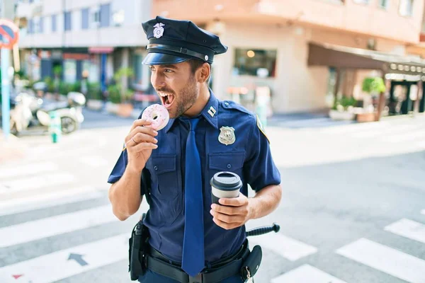 年轻英俊的惊慌失措的警察穿着警服开心地笑着 在镇上街上吃甜甜圈 喝一杯咖啡 — 图库照片