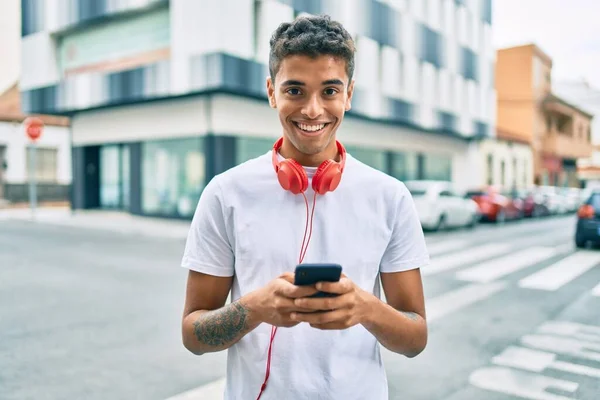 若いラテン系の男は 市内でスマートフォンやヘッドフォンを使用して幸せな笑顔 — ストック写真