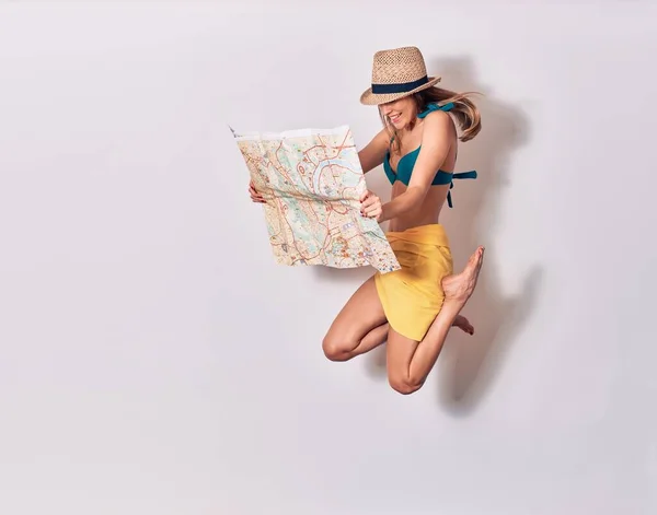 ビキニ姿の若い美少女と夏の帽子が笑顔で幸せ 顔に笑顔でジャンプ隔離された白い背景に都市マップを保持 — ストック写真