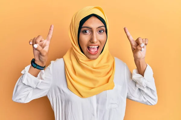 若いですブルネットArab女性身に着けています伝統的なイスラムヒジャーブスカーフ笑顔と驚きと指で指摘し 腕を上げ — ストック写真