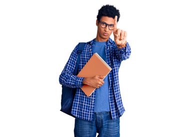 Afrika kökenli Amerikalı genç bir adam, sırt çantası takmış, elinde bir kitapla parmağını kaldırmış ve kızgın bir ifade sergiliyor. 