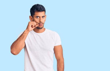 Gündelik kıyafetler giyen genç latin adam ağzı ve dudakları parmaklarıyla fermuar gibi kapalı. gizli ve sessiz, tabu konuşması 