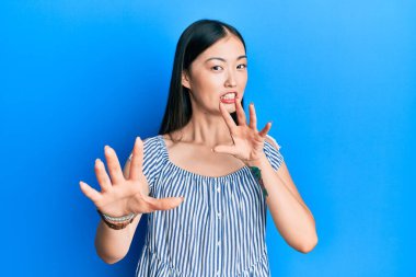 Sıradan çizgili tişört giyen genç Çinli kadın korku ifadesinden korkuyor ve dehşete düşüyor. El hareketlerini durdur, şok içinde bağır. panik konsepti. 