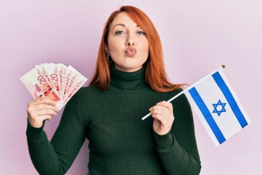 Güzel kızıl saçlı kadın elinde 20 şekel banknot tutuyor ve İsrail bayrağı kameraya bakıyor. Öpücük sallıyor, güzel ve seksi. aşk ifadesi. 