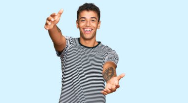 Genç, yakışıklı, Afro-Amerikan bir adam günlük giysiler içinde kameraya bakıyor ve sarılmak için kollarını açmış gülümsüyor. Mutluluğu kucaklayan neşeli bir ifade.. 