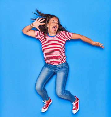 Orta yaşlı, güzel, İspanyol bir kadın. Günlük kıyafetler giyip mutlu gülümsüyor. İzole edilmiş mavi arka planda yüzünde gülümsemeyle zıplıyor