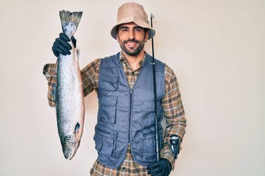 Yüzünde mutlu ve havalı bir gülümsemeyle gülümseyen sakallı ve çiğ somonlu yakışıklı İspanyol bir adam. diş gösterme. 