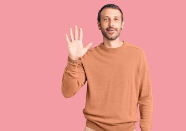 Gündelik kıyafetler giyen genç yakışıklı adam beş numarayı gösterip işaret ederken kendinden emin ve mutlu bir şekilde gülümsüyor.. 