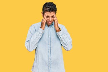 Genç, yakışıklı, Afro-Amerikan bir adam, stres yüzünden elleri başının üstünde gündelik giysiler giyiyor. migren ağrısı. 