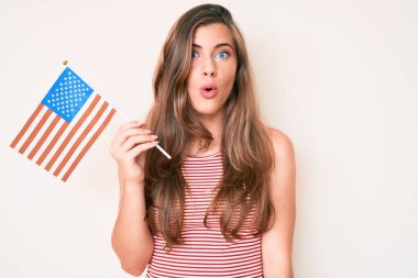 Amerika Birleşik Devletleri bayrağını tutan güzel, beyaz bir kadın ağzı açık kalmış, korkmuş ve şaşırmış bir şekilde şaşkınlık içinde. 
