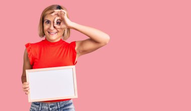 Elinde boş beyaz karatahta tutan genç sarışın kadın gülümsüyor. 