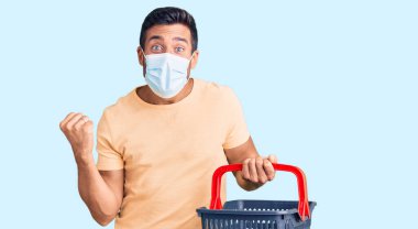 Alışveriş sepeti ve tıbbi maske takan genç İspanyol adam gururla bağırıyor zaferi ve başarıyı kutluyor. 