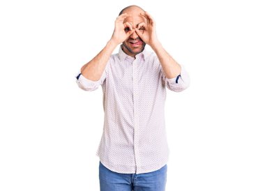 Zarif gömlek giyen genç yakışıklı bir adam dürbün gibi jest yapıyor. Dürbün dilini çıkarıyor, gözler parmaklarından bakıyor. çılgın ifade. 