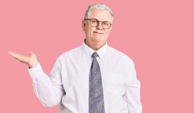 Yaşlı, gri saçlı, iş kıyafetleri giymiş neşeli gülümseyen, avuç içi kameraya bakan bir adam.. 