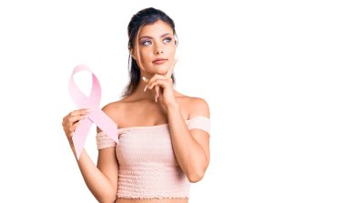 Genç ve güzel bir kadın elinde kanser farkındalığı pembe kurdele ciddi bir yüz eli çenesinde soruyu düşünüyor kafa karıştırıcı bir fikir hakkında düşünceli. 