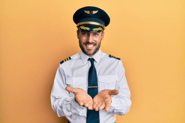 Avuç içleri birbirine gülümseyen ve el hareketi yapan, uçak pilotu üniforması giyen yakışıklı İspanyol. Bekleme ve koruma 