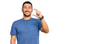 Dövmeleri olan, sıradan kıyafetler giyen, gülümseyen, kendine güvenen, el hareketi yapan, parmakları küçük gösteren ve kameraya bakan yakışıklı bir adam. ölçüm kavramı. 