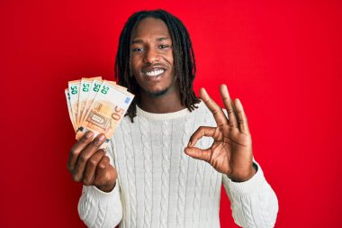 Elinde 50 avroluk banknotlar tutan Afrika kökenli Amerikalı adam parmaklarıyla imza atıyor, gülümsüyor ve mükemmel bir sembol oluşturuyor. 