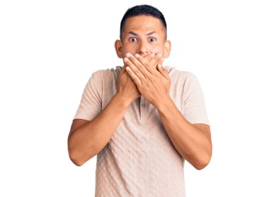 Gündelik kıyafetler giyen genç, yakışıklı Latin adam yanlışlıkla elleri ile ağzını kapatırken şok oldu. gizli kavram. 