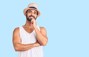 Gündelik yaz şapkası takan genç İspanyol adam kameraya kollarını kavuşturup gülümseyerek ve çenesini kaldırarak bakıyor. Olumlu düşünmek. 