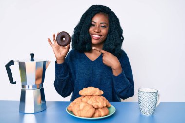 Güzel Afrikalı kadın kahvaltısını yapıyor çikolatalı donutla gülümsüyor. 