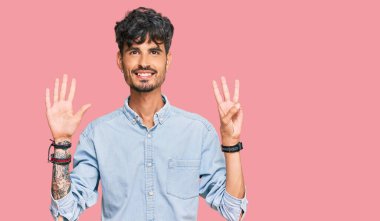 Gündelik kıyafetler giyen genç İspanyol adam sekiz numarayı gösterip işaret ederken kendinden emin ve mutlu bir şekilde gülümsüyor.. 