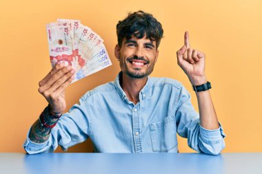 Elinde Kolombiya pezosu olan genç İspanyol bir adam bir fikir veya soruyla gülümsüyor ve gülümsüyor. 