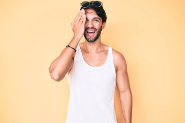 Yaz görünüşü takan yakışıklı İspanyol bir adam ve güneş gözlüğü bir gözünü eliyle kapatıyor, yüzünde kendine güvenen bir gülümseme ve şaşırtıcı bir duygu var.. 