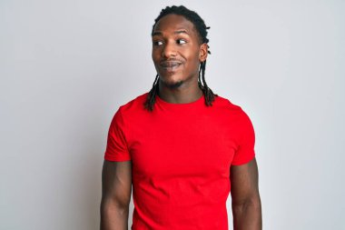 Saçları örgülü, günlük kıyafetler giyen, gülümseyen ve kafasını çeviren Afro-Amerikan bir adam.. 