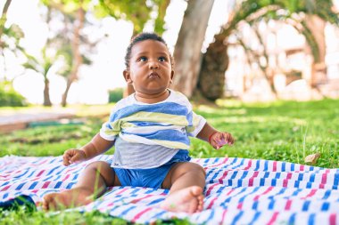 Sevimli Afro-Amerikan çocuk parkta çimlerin üzerinde oturuyor..