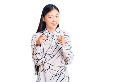 Gündelik tişört giyen genç, güzel Çinli bir kadın mutlu ve komik yüzüyle kamerayı işaret ediyor. iyi enerji ve titreşimler. 