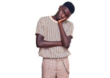 Genç, Afro-Amerikalı bir adam günlük kıyafetler giyip kollarını kavuşturup depresyondan sıkılmış ve yorgun görünüyor.. 