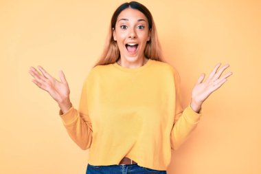 Sarı arka planda genç esmer kadın zaferi mutlu bir gülümseme ve kaldırılmış ellerle kazanan ifadeyle kutluyor. 